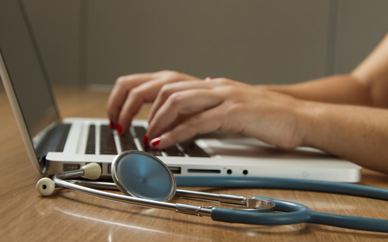 Hands typing on a laptop next to a stethoscope